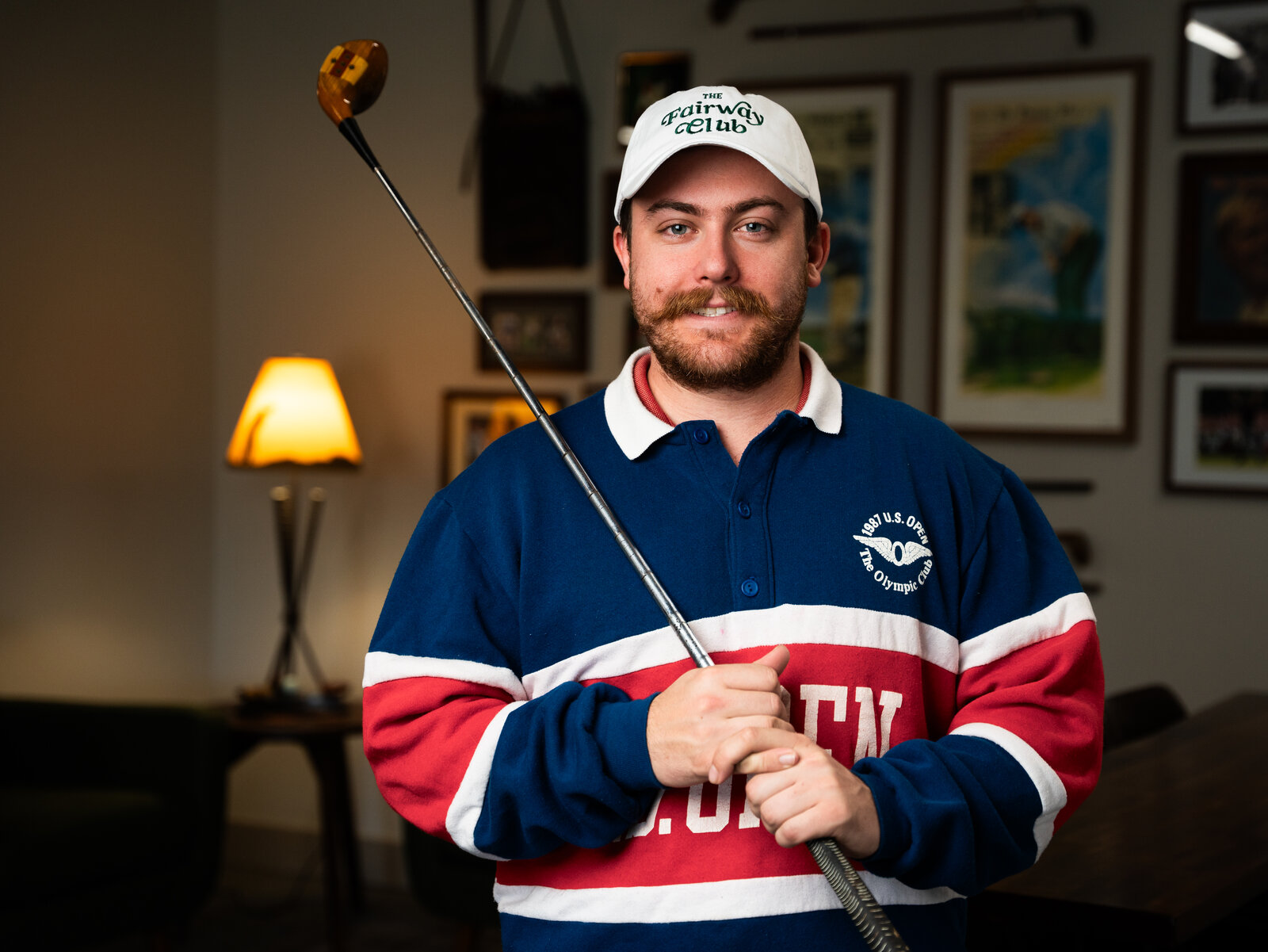 Logan Dahmer, founder of Fairway Club, holding a vintage persimmon driver in a 1987 U.S. Open polo at his Lee's Summit, Missouri studio
